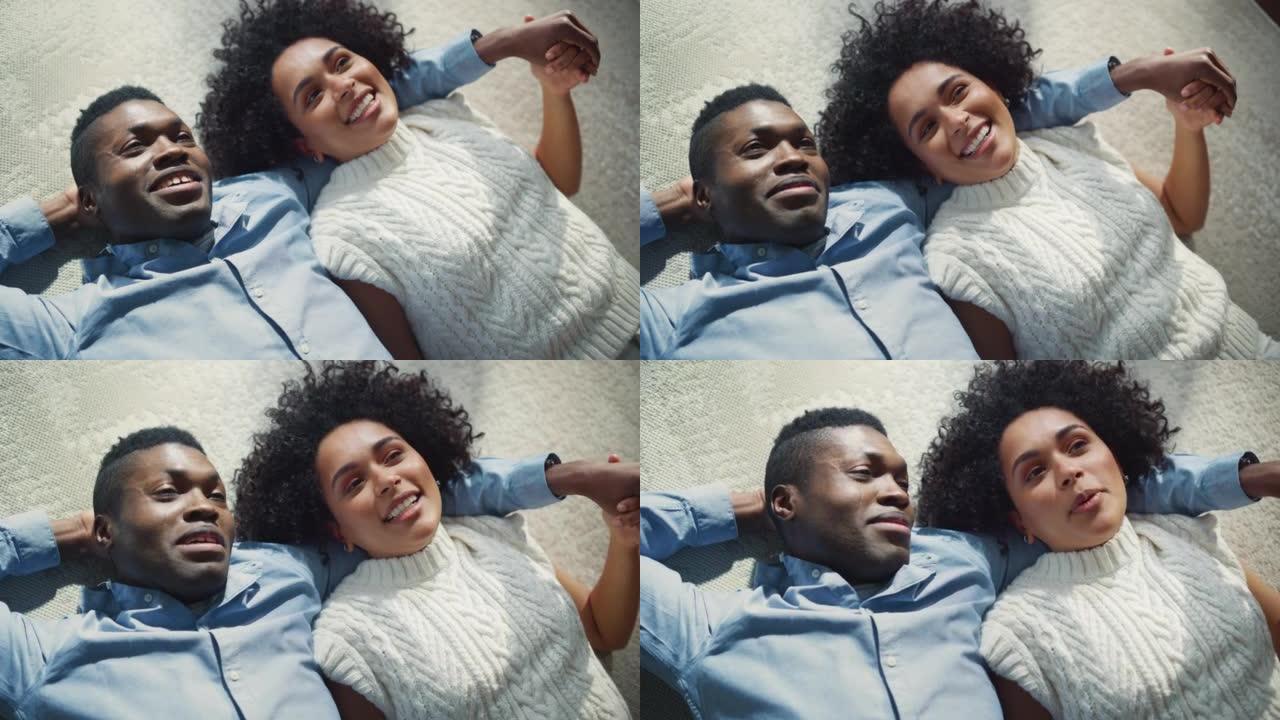 快乐的黑人夫妇在地板上拥抱时做梦和谈论未来的慢动作镜头。恋爱中的男朋友和女朋友在一起。顶视图