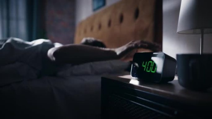 男人醒来后关掉闹钟。早起的有生产力的人准备开始充满新冒险的一天。床头床头柜专注于显示四点钟的时钟。卧