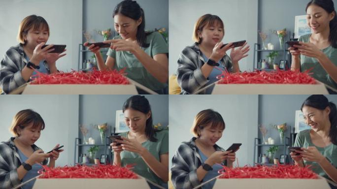 快乐亚洲女士朋友从在线市场打开纸板箱包装拍照以进行反馈评论，以在家中客厅购买网站社交媒体。