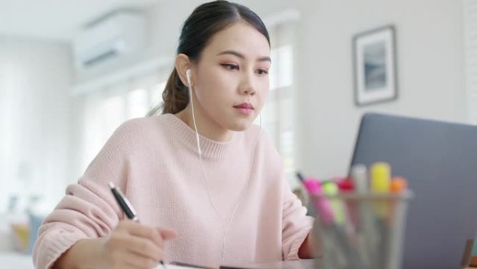 坦率的年轻有吸引力的亚洲女员工戴着耳机听数字在线课程发展计划在隔离社会距离在家里技能提高技能学校课程