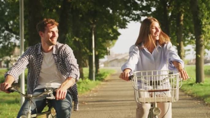 年轻无忧无虑的幸福情侣的真实照片在一个阳光明媚的日子里，他们很开心，喜欢一起在绿色公园骑自行车。