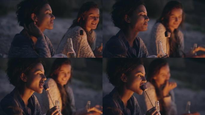 4k视频片段，一名年轻女子与朋友坐在沙滩上，吃烤棉花糖