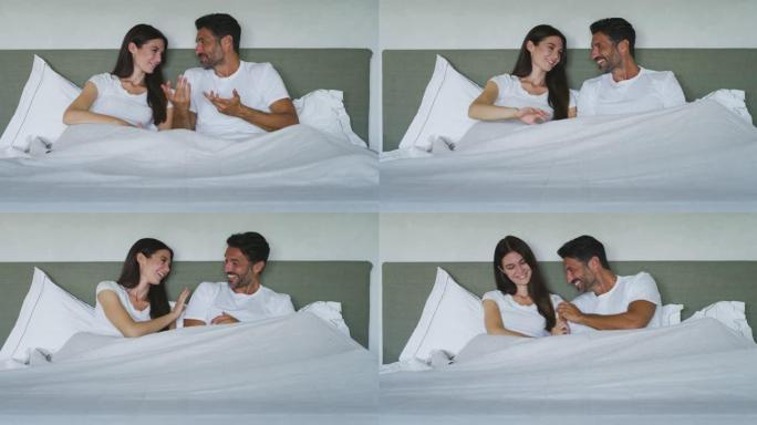 穿着睡衣的年轻新婚夫妇的真实照片是在卧室的床上一起休息时说话和笑的乐趣。早上刚醒来。