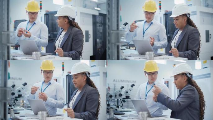 亚洲技术人员和非裔美国工程师戴着安全帽，在工厂使用笔记本电脑。讨论工业机器零件，将零件与草拟的蓝图进