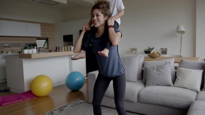 快乐的拉丁美洲妇女在蹲下时在家锻炼，用儿子作为额外的体重