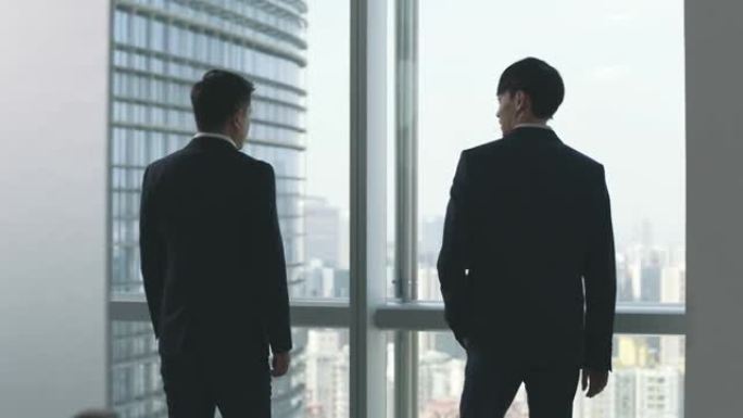 两名亚洲商人站在窗边谈话办公室