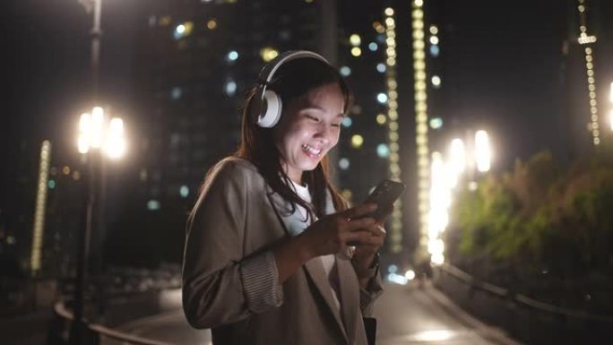 亚洲女性晚上使用带耳机的智能手机