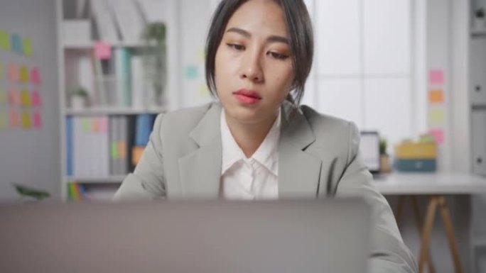 年轻的亚洲女商人坐在办公室里，笔记本电脑过度劳累，倦怠综合症。
