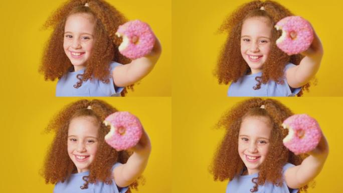 红头发女孩在黄色背景下吃甜甜圈的工作室镜头 -- 慢动作镜头