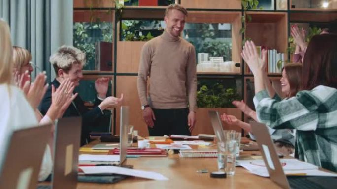 快乐的年轻白人男性老板，执行经理告诉团队在办公室餐桌会议上庆祝成功的好消息。