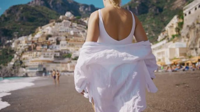 穿着白衬衫的SLO MO女人在波西塔诺村的海滩上行走