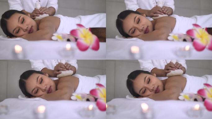 年轻的亚洲妇女躺在床上放松，在水疗沙龙里做热石按摩