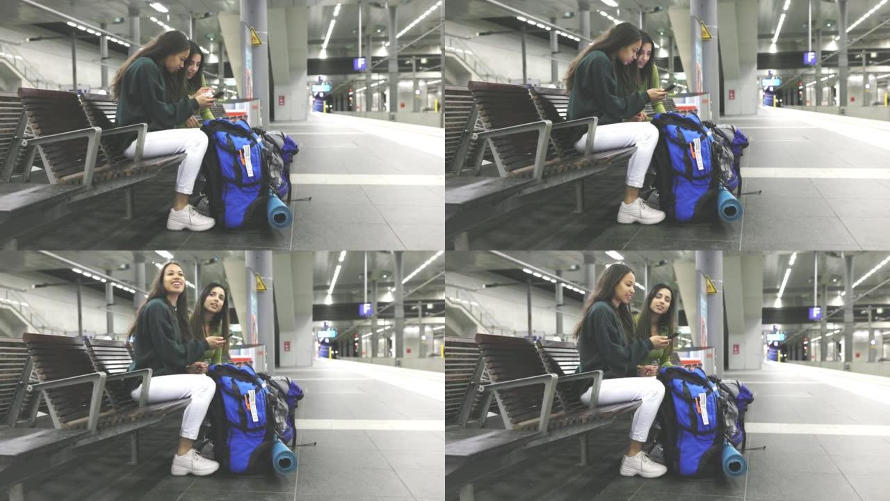 两名年轻女性旅行者在车站等火车时使用智能手机
