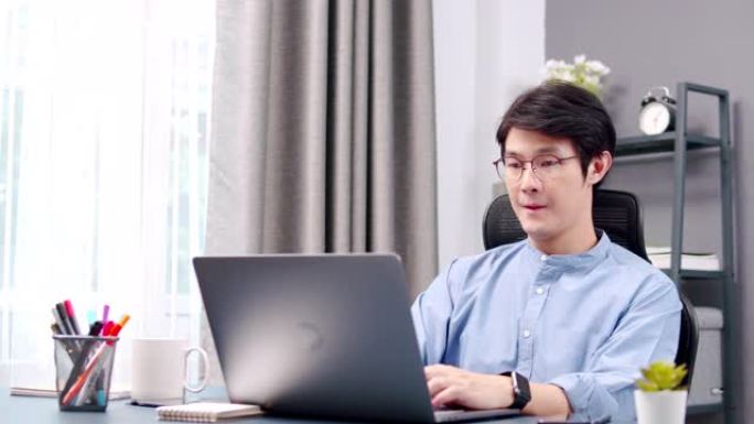 宽镜头有吸引力的亚洲商人在笔记本电脑上工作或打字，完成工作后关闭笔记本电脑。成人在家工作或远程工作时