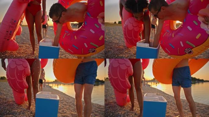 SLO MO年轻人在日落时从海滩上的冷却器中喝冷饮