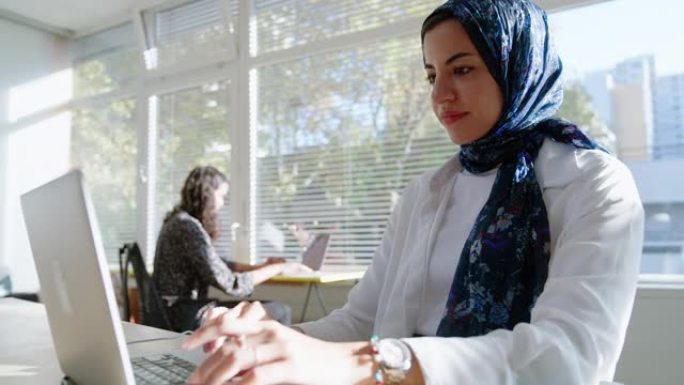 Mulsim女士戴着头巾在笔记本电脑上工作，坐在办公场所
