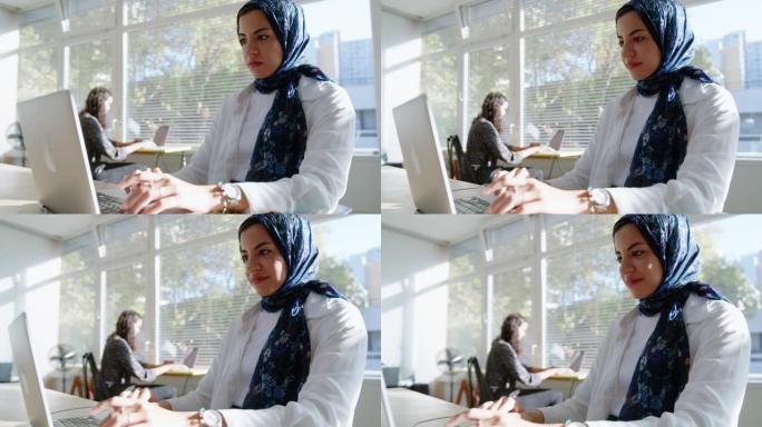 Mulsim女士戴着头巾在笔记本电脑上工作，坐在办公场所