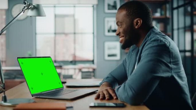 英俊的黑人非洲裔美国专家在笔记本电脑上通过视频通话聊天，并在家庭客厅显示绿屏模型。自由职业者在社交网