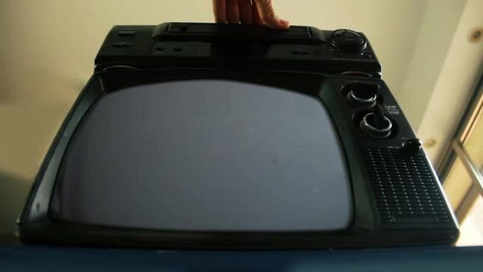 男性手将VHS插入VCR和带有绿色屏幕的旧电视中。