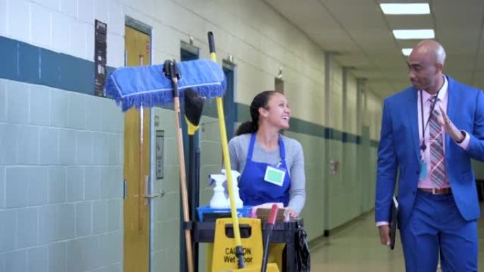 Teacher walks through school hallway, waves to cus