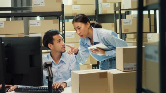 快乐的亚洲男人和女士伴侣穿正式衬衫坐在办公桌前电脑和条码机扫描仪讨论库存细节客户在线数据交付在仓库。
