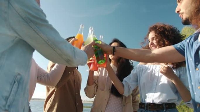 快乐的朋友在海滩上碰碰瓶子和喝酒的慢动作肖像