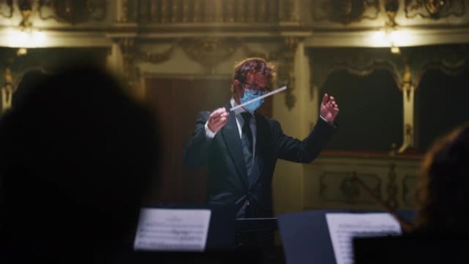 指挥交响乐团指挥的电影镜头，表演者戴着医用防护面具，在经典剧院演奏小提琴，大提琴和小号