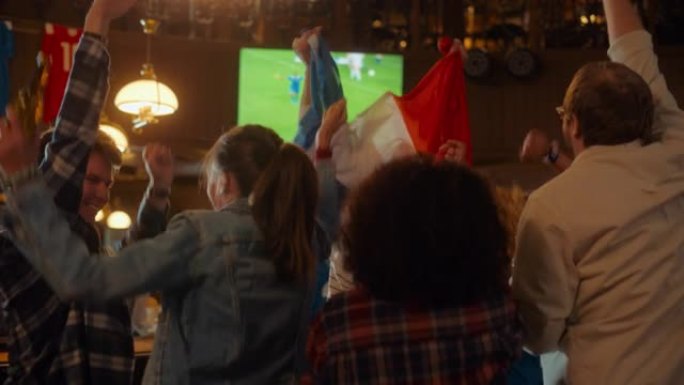 一群足球迷在体育酒吧直播足球比赛时欢呼、尖叫、举手和跳跃。穿着蓝色衬衫的球员进球，朋友们庆祝。慢动作