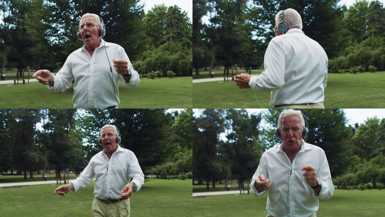 一个活跃的老人在公园里活泼跳舞的肖像，用耳机听音乐。快乐开朗的老年男性，穿着白衬衫享受生活，伴随着他