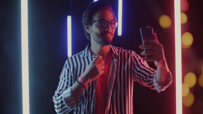 在带有霓虹灯照明的黑色背景的在线视频通话中，年轻人说话的肖像显示竖起大拇指的手势