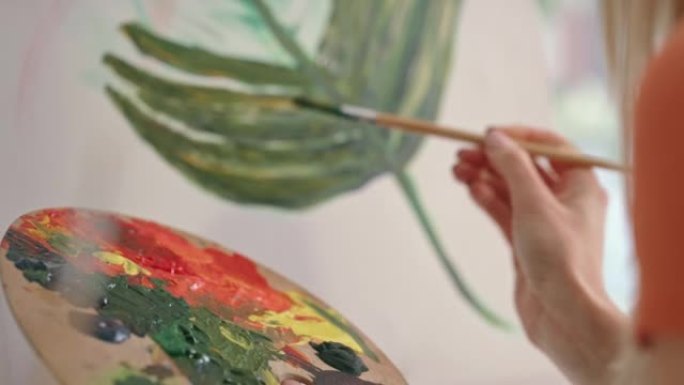 艺术家在画布上绘画的特写镜头，同时将画笔浸入调色板上。具有创造力的艺术人物，喜欢学习如何绘画丰富多彩