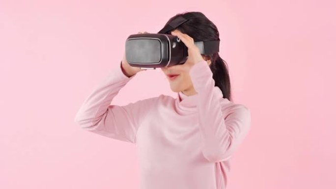 亚洲少女戴着虚拟现实耳机，在虚拟现实体验中站在粉红色背景和触摸空气时兴奋地打手势。技术