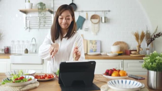 年轻女子快乐跳舞烹饪沙拉，快乐在厨房