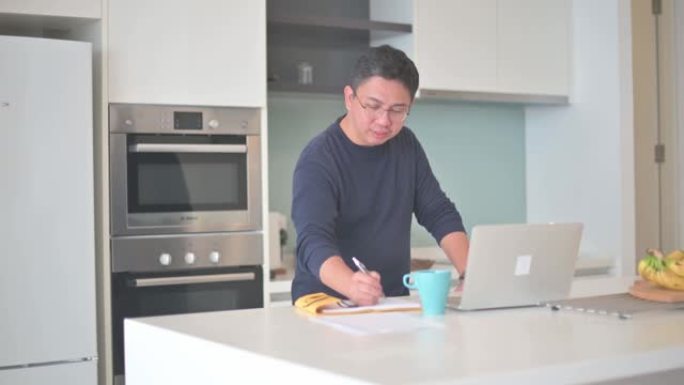 亚洲中国男性在家工作，在厨房柜台使用笔记本电脑视频通话
