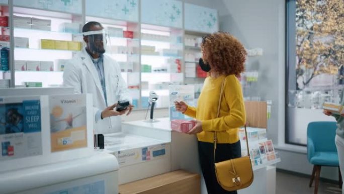药房药店收银台: 专业的戴面罩的黑人药剂师向戴面罩的不同客户群体出售药品，使用非接触式付款。冠状病毒