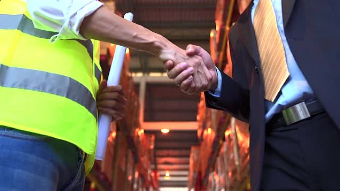 商务人士和工程师的握手展示了公司/组织之间签署协议或合同的协议，背景是仓库。
