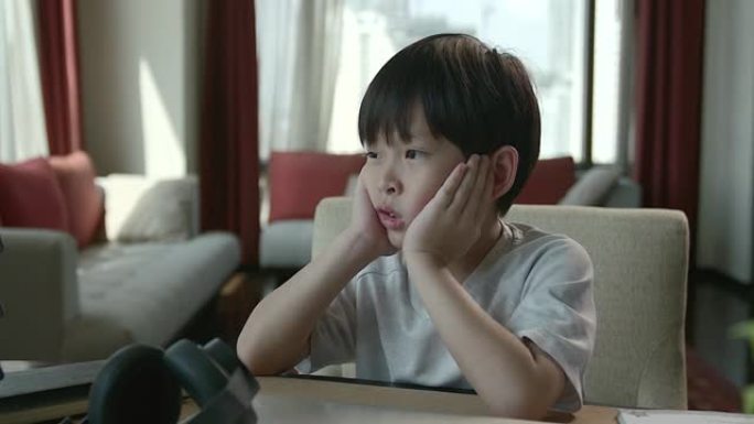 一个坐在网上学习的亚洲男孩感到无聊，看着窗外，他不得不适应学习一种新的常态，即人们由于Covid 1