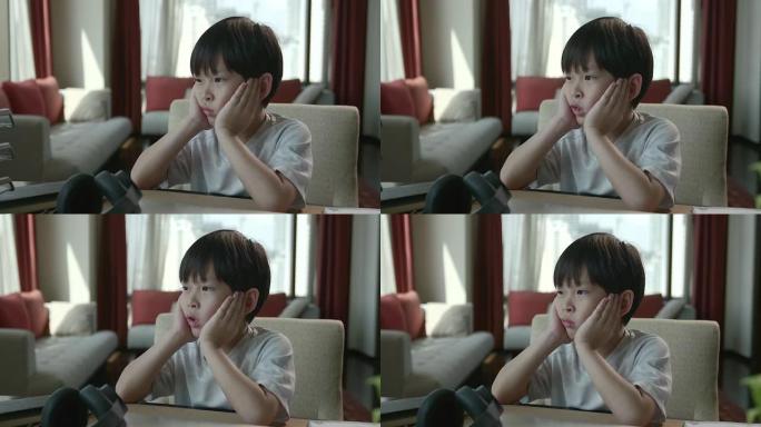 一个坐在网上学习的亚洲男孩感到无聊，看着窗外，他不得不适应学习一种新的常态，即人们由于Covid 1