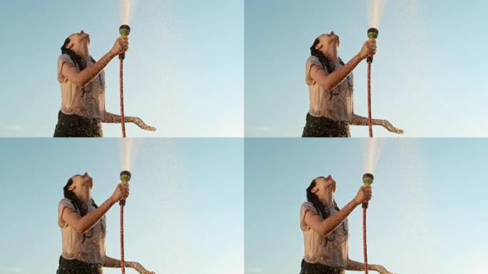 超级SLO MO年轻女子使用花园软管向自己喷水