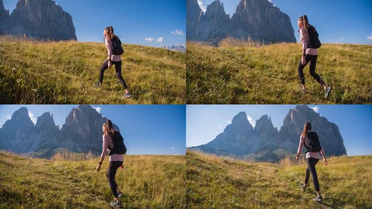 女人很活跃，在雄伟的山脉前的草山上徒步旅行