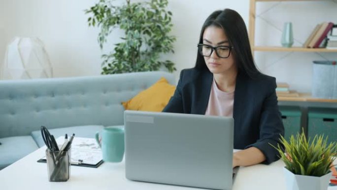 有动力的亚洲女企业家在笔记本电脑上工作，在家桌上喝茶