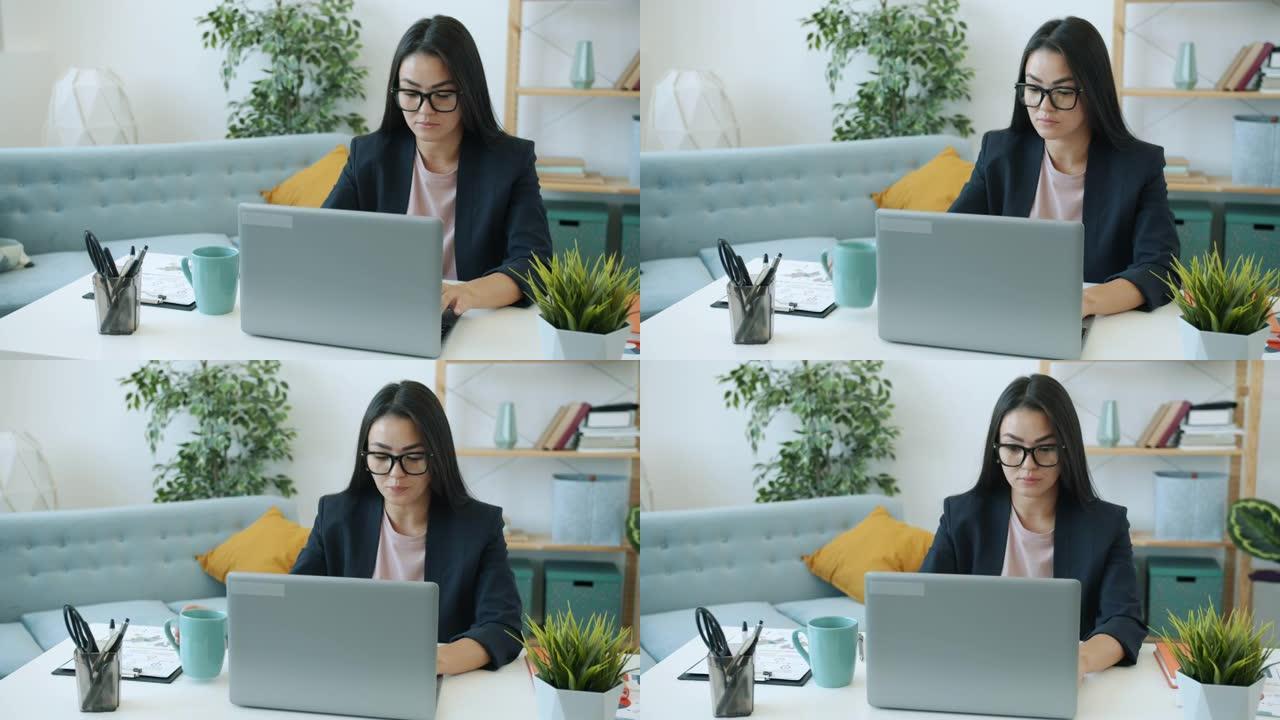 有动力的亚洲女企业家在笔记本电脑上工作，在家桌上喝茶