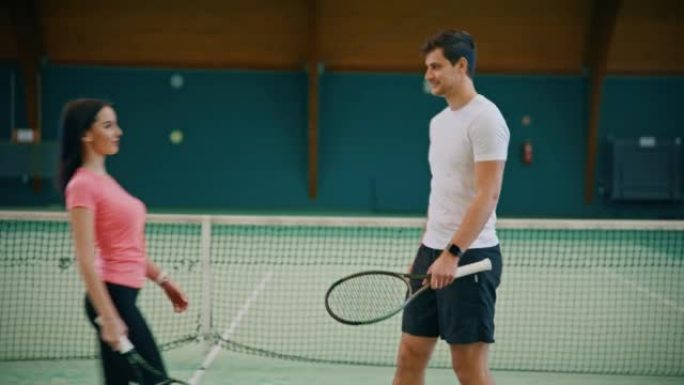 年轻的男教练和女子在网球场上站在一起
