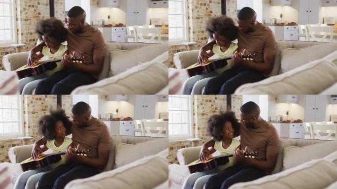 非裔美国父亲和他的女儿坐在沙发上一起弹吉他