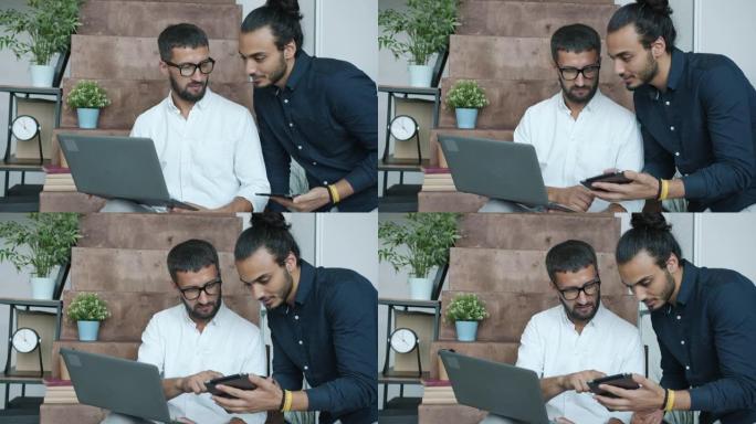 在现代创意办公室中使用笔记本电脑和平板电脑交谈的男性同事分享想法