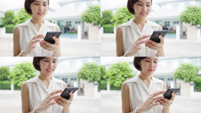 迷人的年轻亚洲女商人使用手机检查社交媒体互联网，在城市的街道上与朋友聊天。