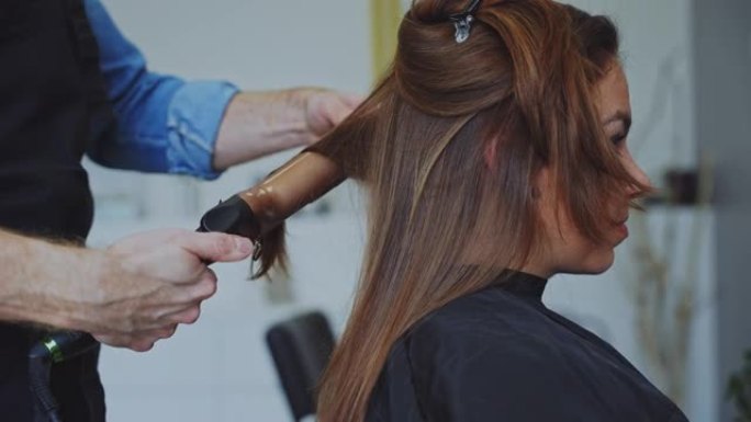 发型师在美容院用铁棒卷曲女性客户的头发