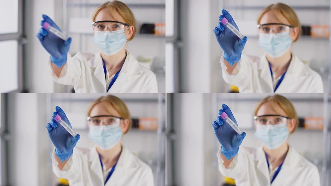 拉焦点肖像的女实验室研究人员戴着安全眼镜和面罩，拿着含有PCR拭子测试的试管，以慢镜头拍摄