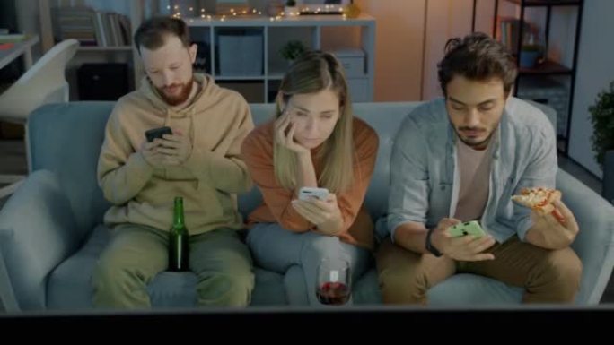 使用智能手机的多元文化朋友在黑暗的公寓里喝酒吃披萨，晚上看电视