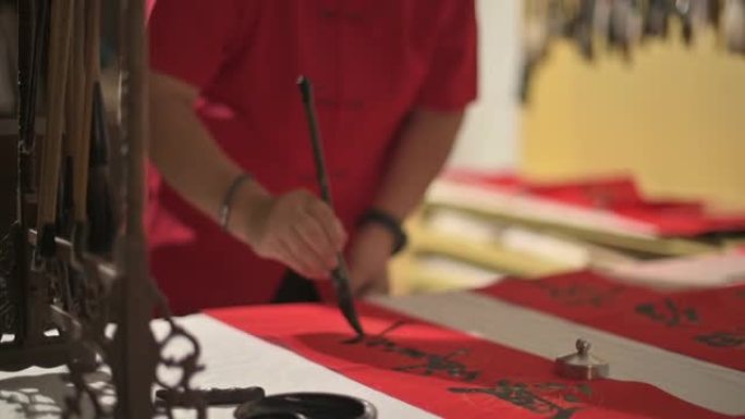 亚洲中国男性的手为即将到来的农历新年庆祝活动而练习中国书法，目的是通过将其写在红色纸上来实现繁荣和良